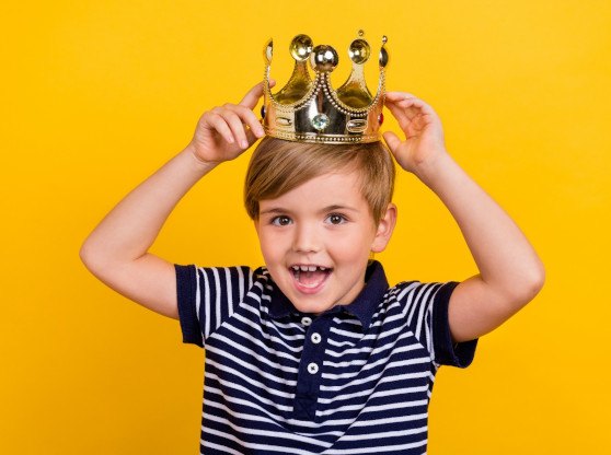 Young boy in striped shirt wearing toy crown with yellow background