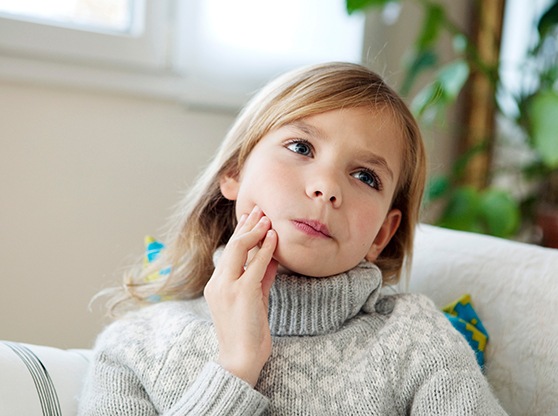 Little girl with sweater sitting on couch with tooth pain