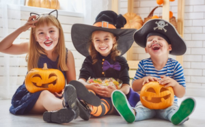 Three children in Halloween costumes sitting with a bowl of candy