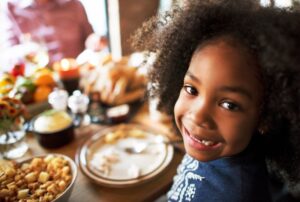 little kid smiling and sitting at the table with Thanksgiving dinner